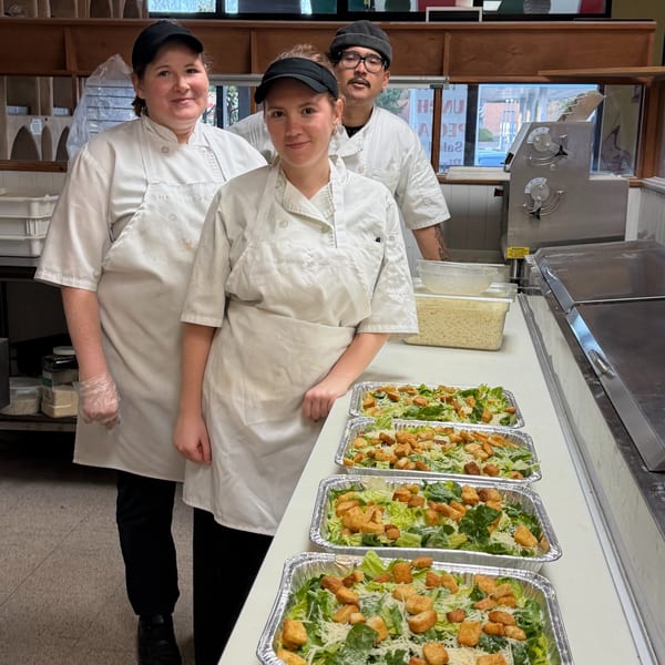 Three Cerello's Pizza chefs in white uniforms stand behind a counter with Caesar salads.
