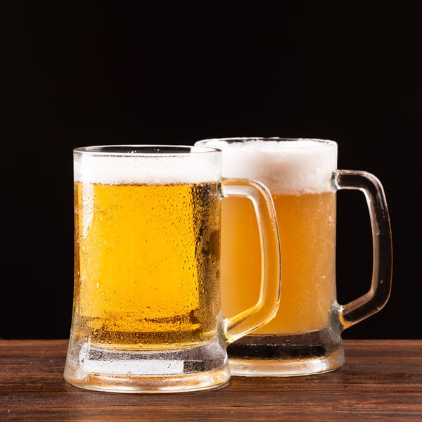 Two frosty mugs of Cerello's golden beer with foamy heads sit on a dark wooden table.