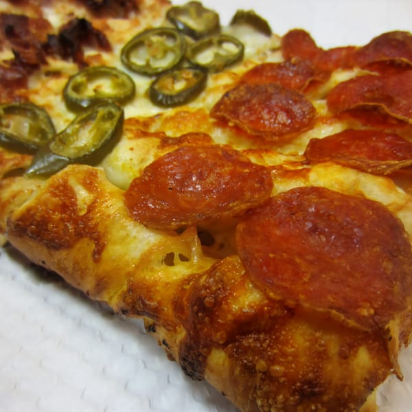 Close-up of a Cerello's Pizza slice with pepperoni, jalapeños, and bacon, showing a golden crust.
