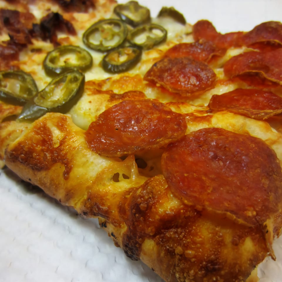 Close-up of a Cerello's Pizza slice with pepperoni, jalapeños, and bacon, showing a golden crust.