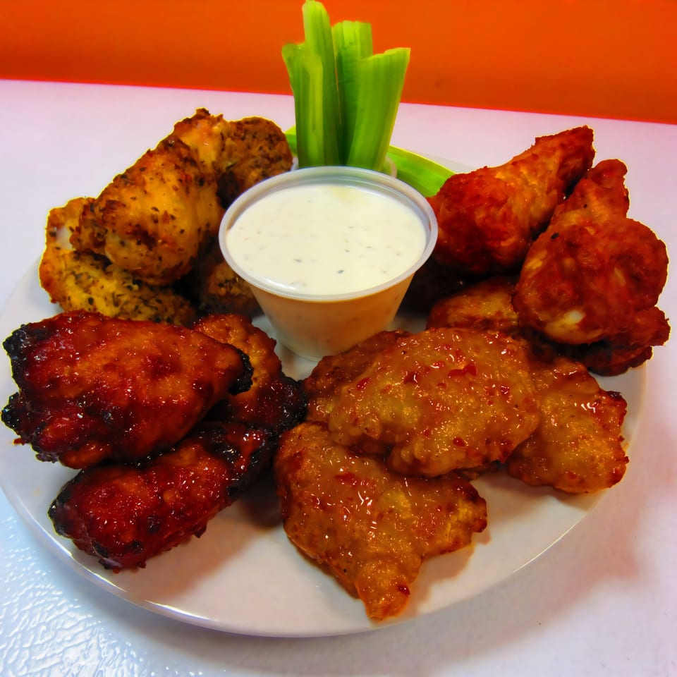 A plate of Cerello's Pizza chicken wings in various sauces with celery sticks and ranch dip.