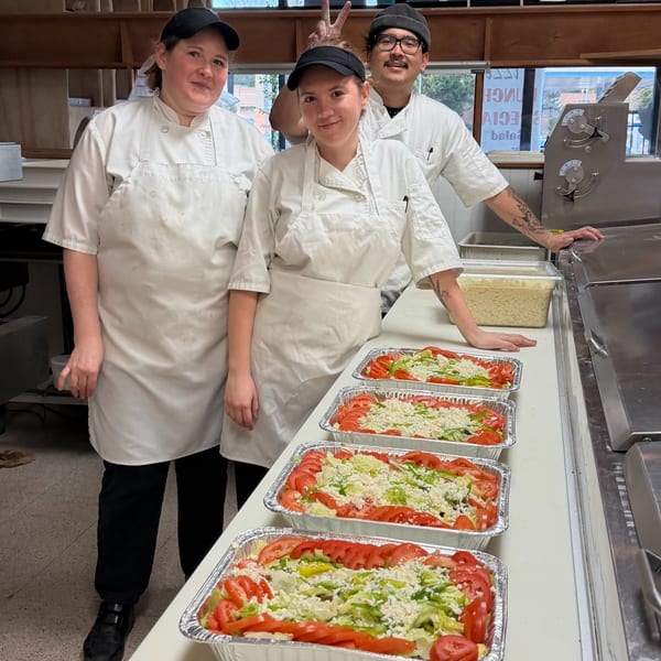 Three Cerello's Pizza chefs, two women and one man, stand proudly behind several large salads.